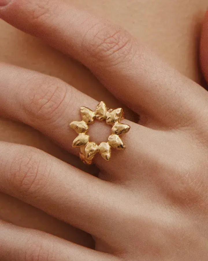 Gold Hélia ring with sunray petals and molten surface, worn on a finger.