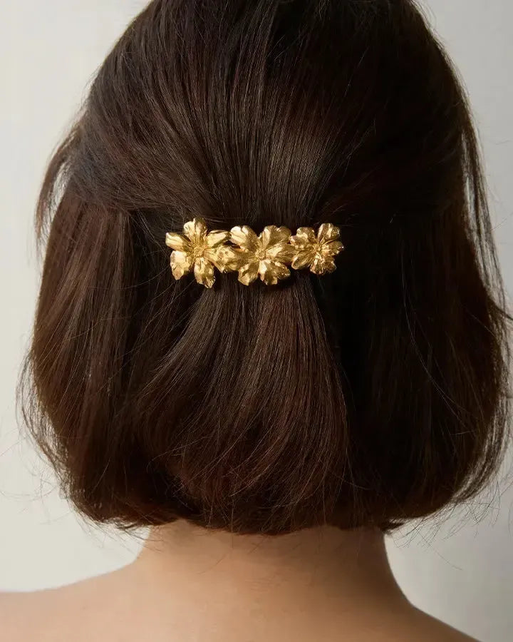 Pinza para el pelo dorada Rosaria con tres flores delicadas en flor, sobre cabello castaño oscuro.