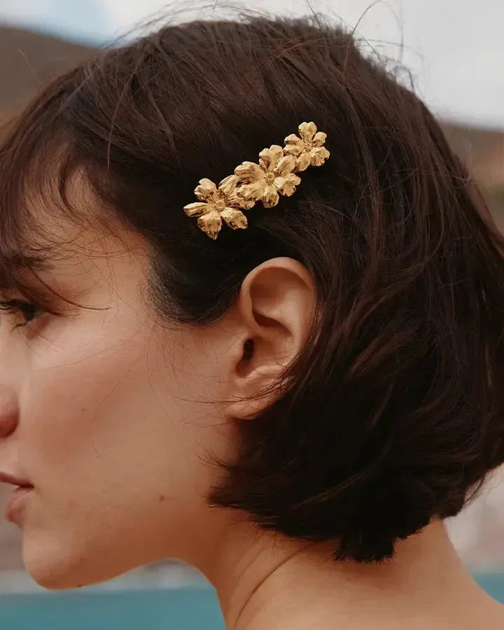 Pinza para el pelo dorada Rosaria con tres flores delicadas en flor, en cabello castaño corto.