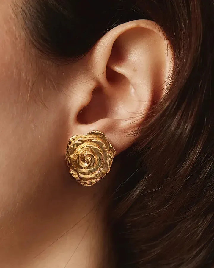Gold rose flower earring with voluminous, hammered petals on an ear.