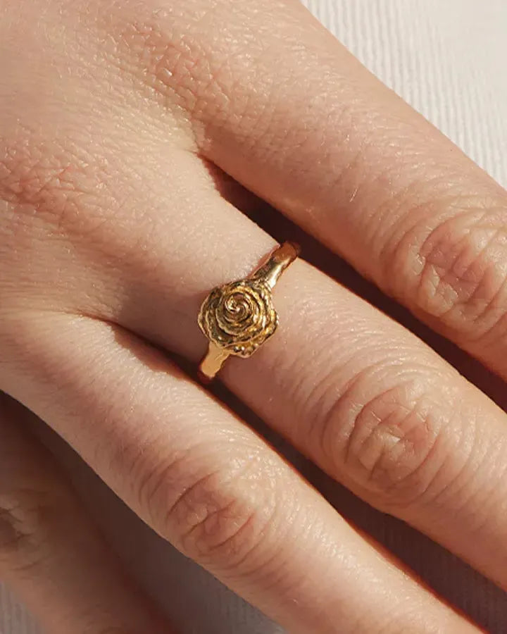 Anello Rosie Mini dorato con un design a fiore di rosa testurizzato, su un dito.