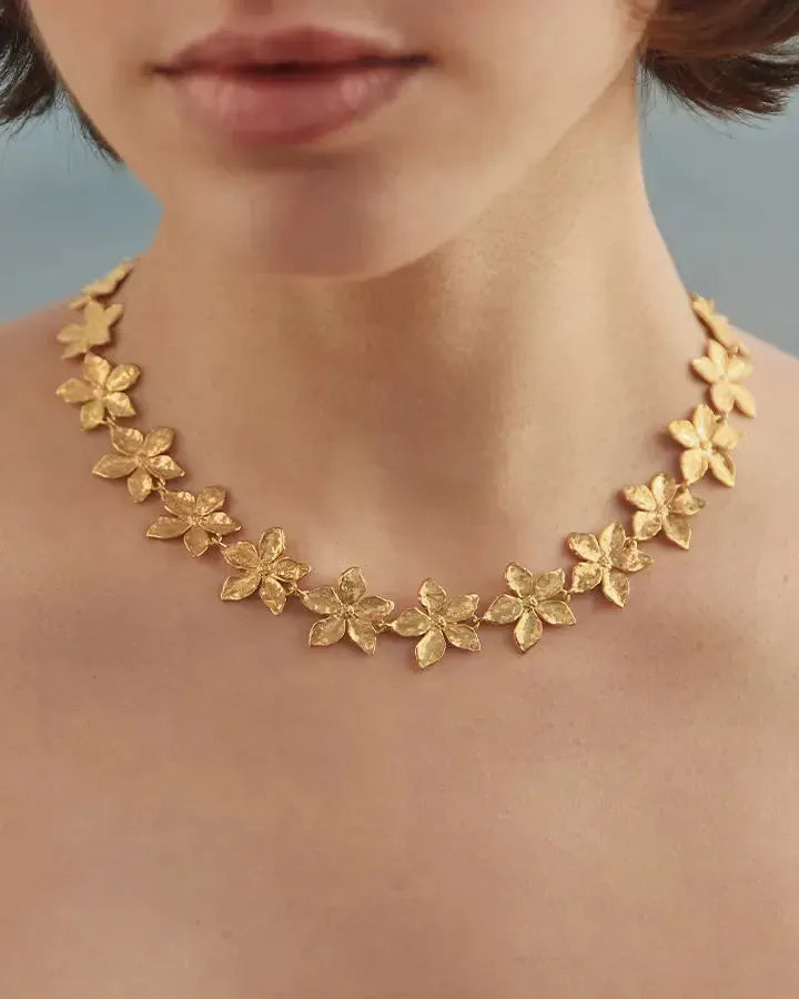 Gold Thalla choker with hammered five-petal floral links on a woman's neck.