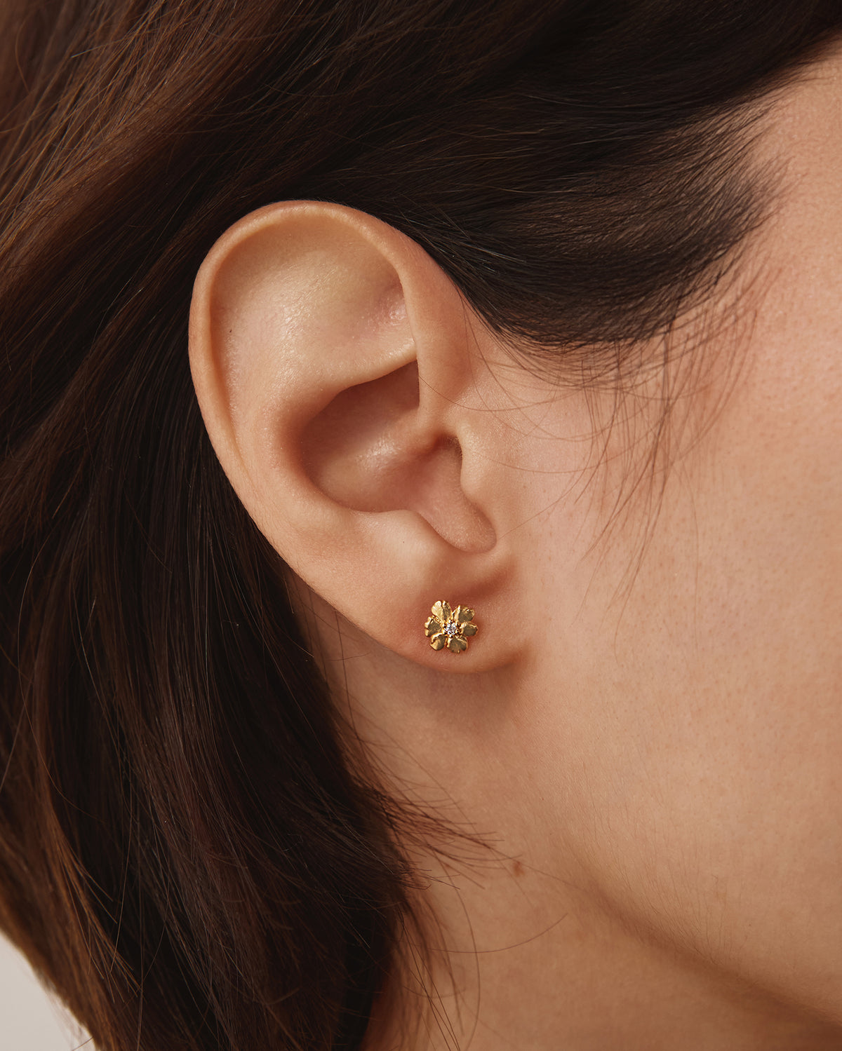 Gold Aleli floral stud earrings featuring a delicate blooming flower design with a luminous white stone center.