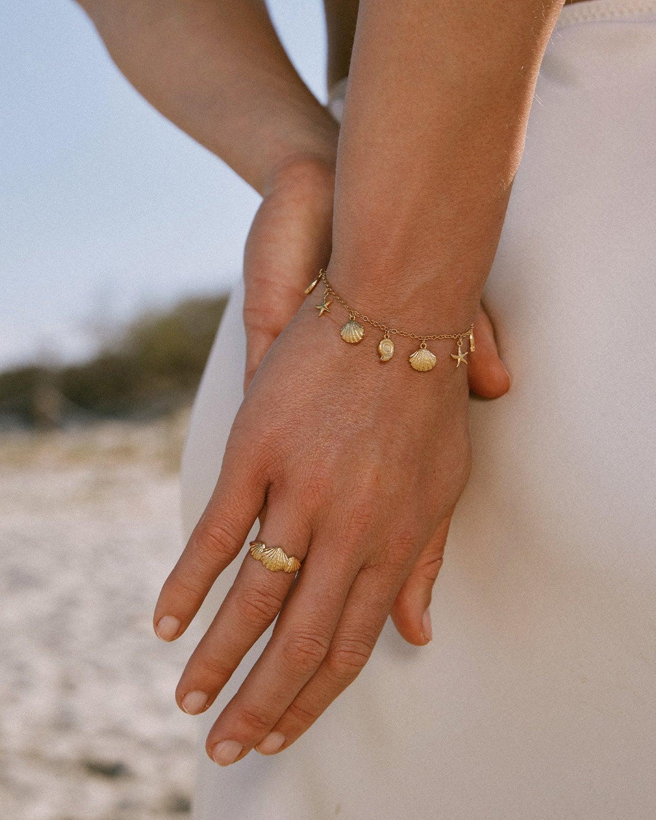 Delicada pulsera de cadena dorada con cinco pequeños colgantes de concha y estrella de mar de inspiración marina, en la muñeca de una mujer.