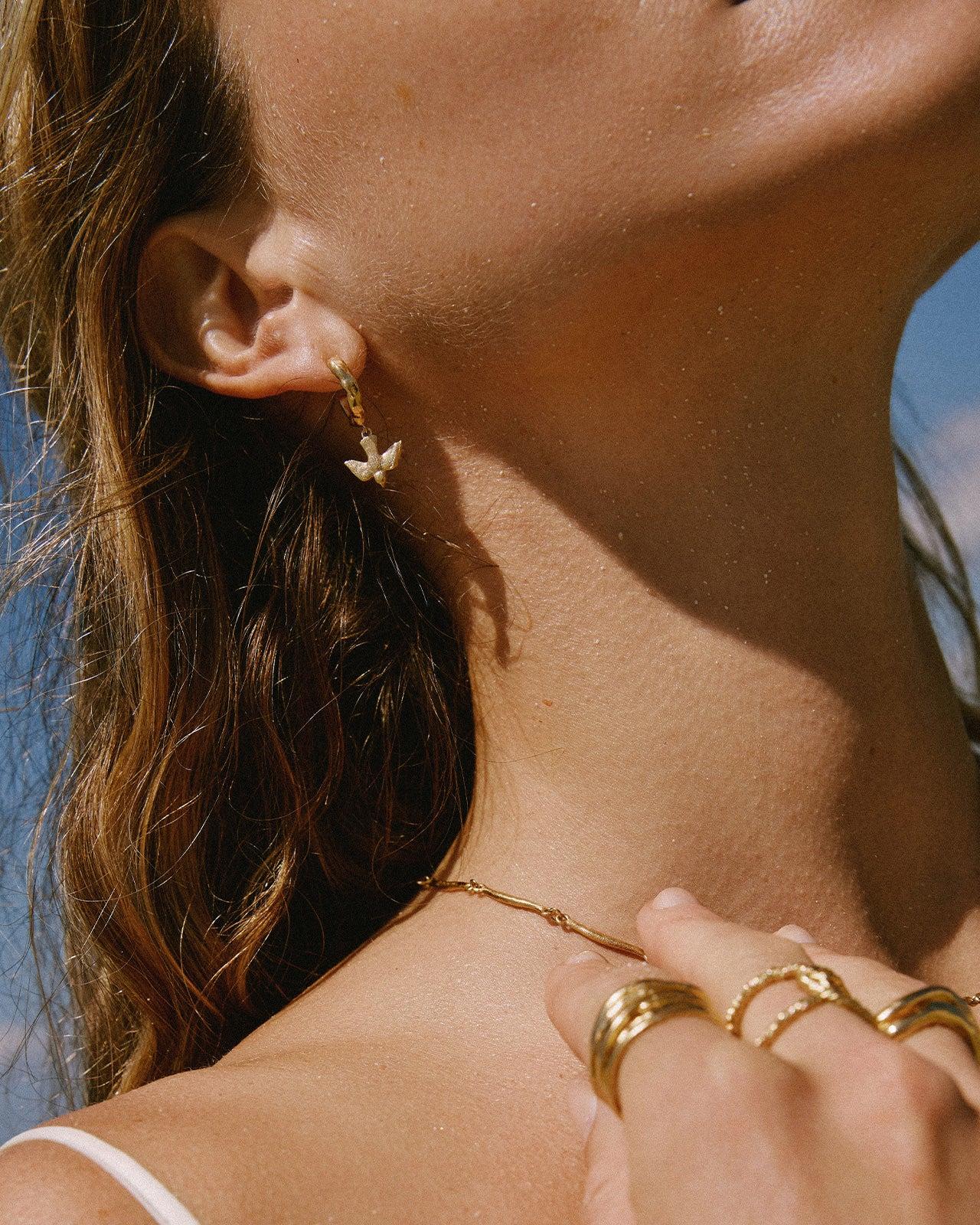 Gold mini-hoop earrings featuring a delicate, detailed flying bird pendant with outstretched wings.
