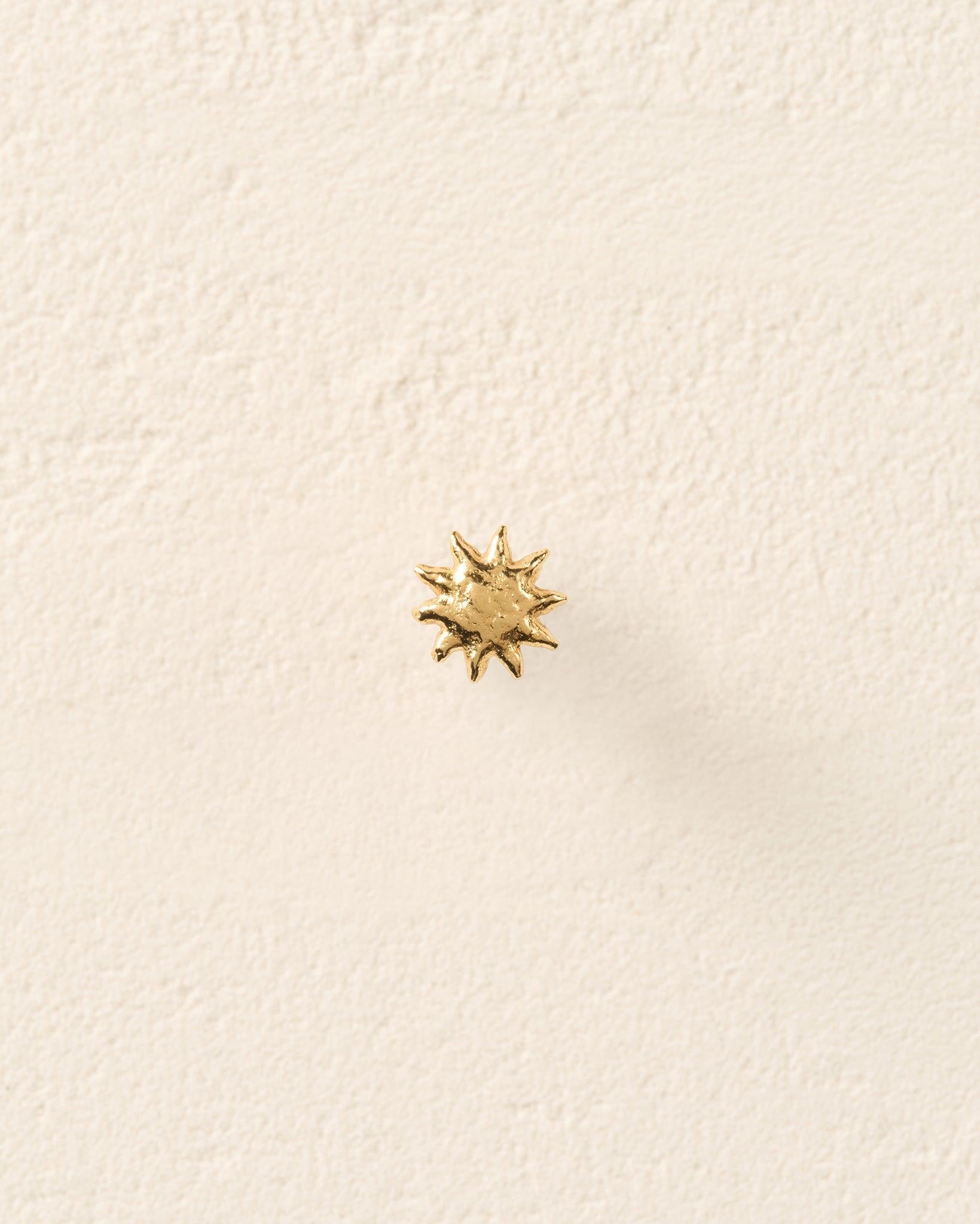 Small gold sun stud earring with a sculpted, domed, and hammered surface.