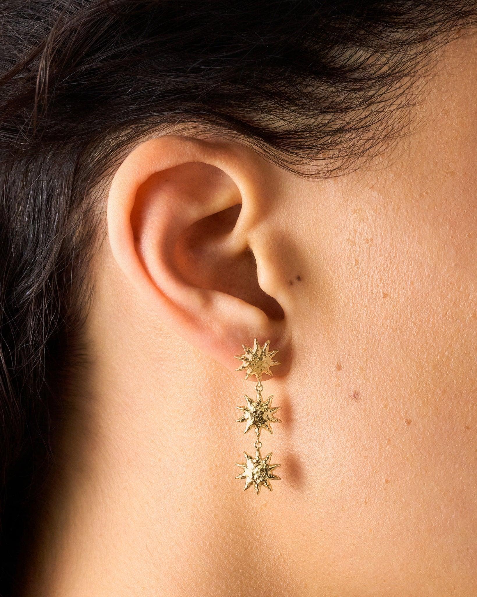 Gold Soléos sun drop earrings with three cascading, hammered, domed suns on a woman's ear.
