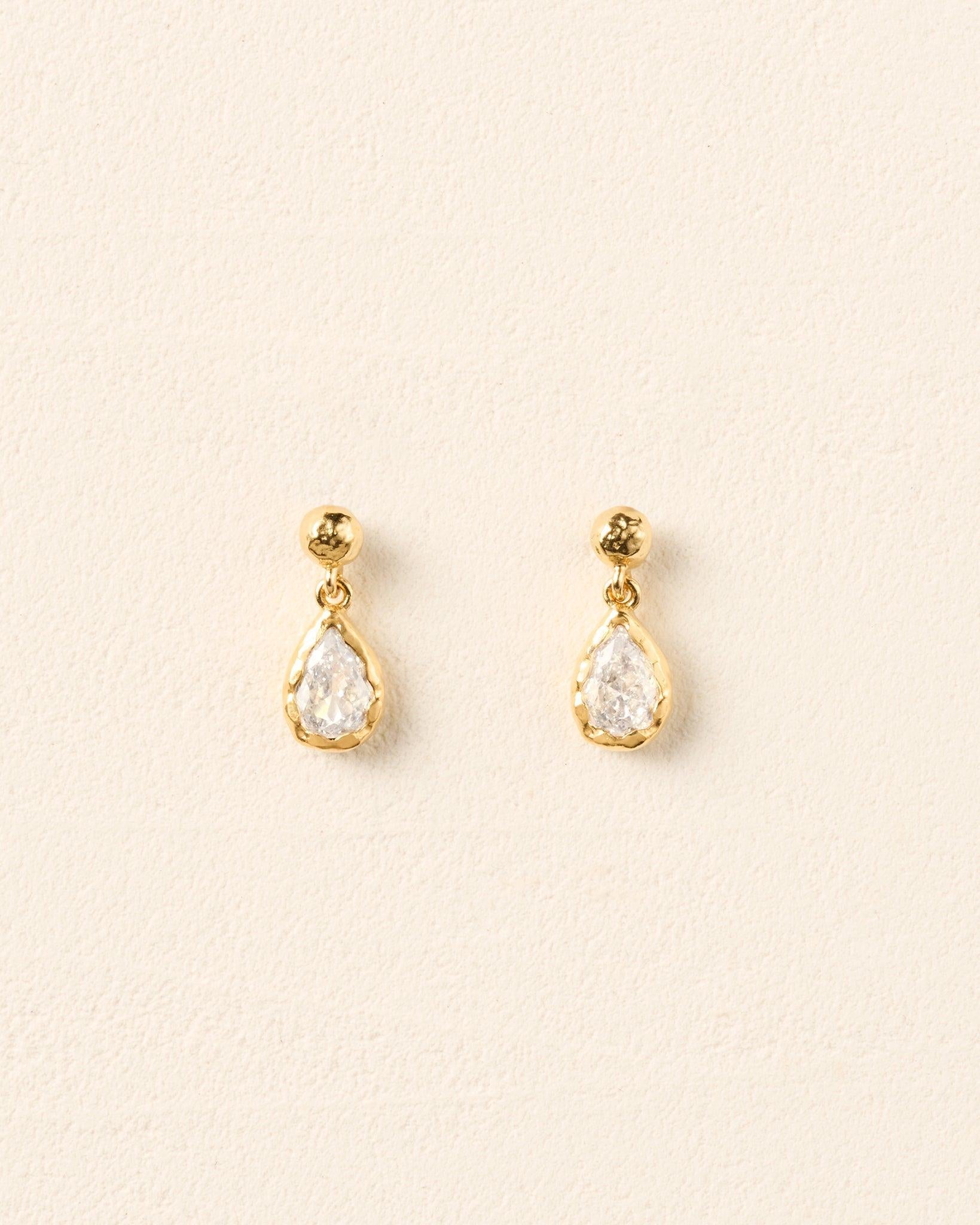 Lyséa drop earrings featuring pear-shaped white stones set in textured gold, suspended from hammered gold studs.