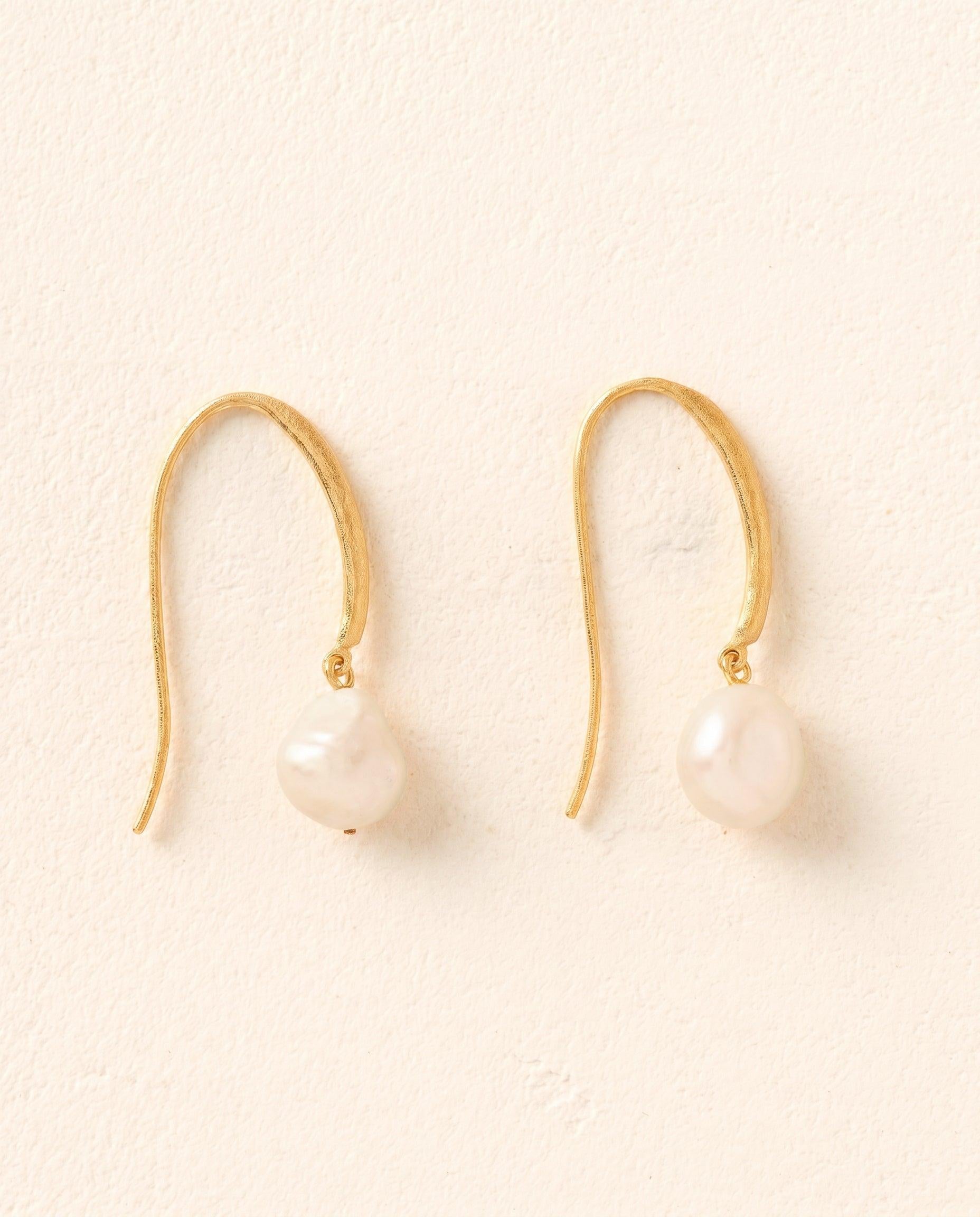 Symi earrings: Luminous white pearls suspended from softly hammered, slender gold hooks.