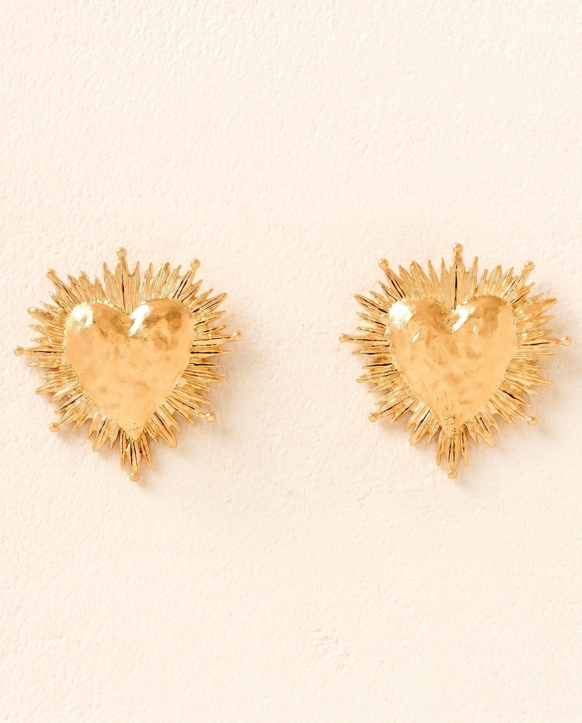 Two gold heart earrings with hammered centers and intricate sunburst designs.