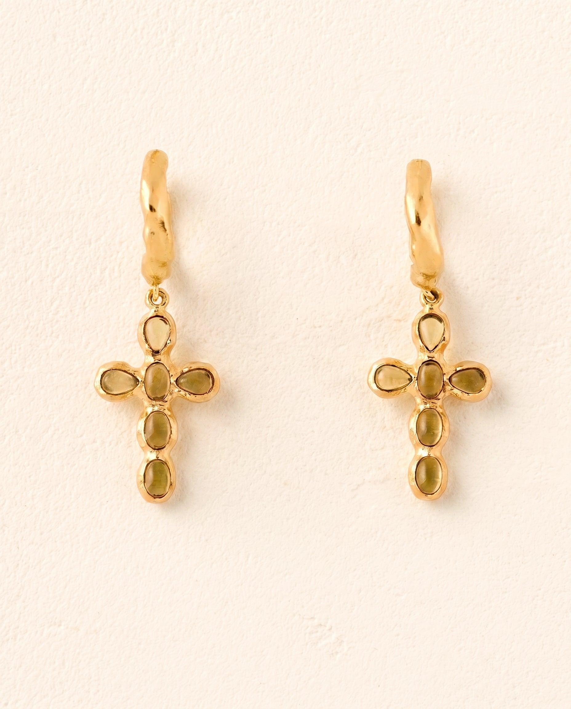 Pair of Nexa gold mini hoop earrings with cross pendants featuring oval green stones.