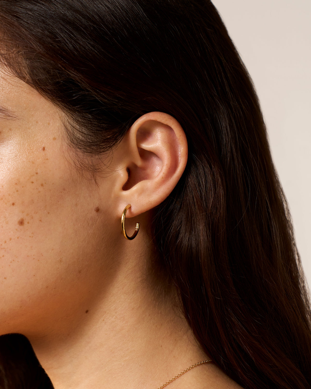 Elena Large gold hoop earring worn in the ear lobe.