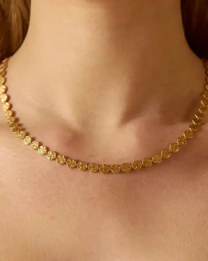 Caius necklace: continuous design of small, hammered gold discs on a woman's neck.