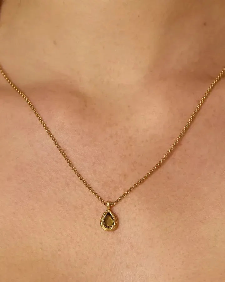 Collier Lysia à pierre vert foncé en forme de goutte, sertie dans un métal doré texturé, sur une chaîne dorée fine.