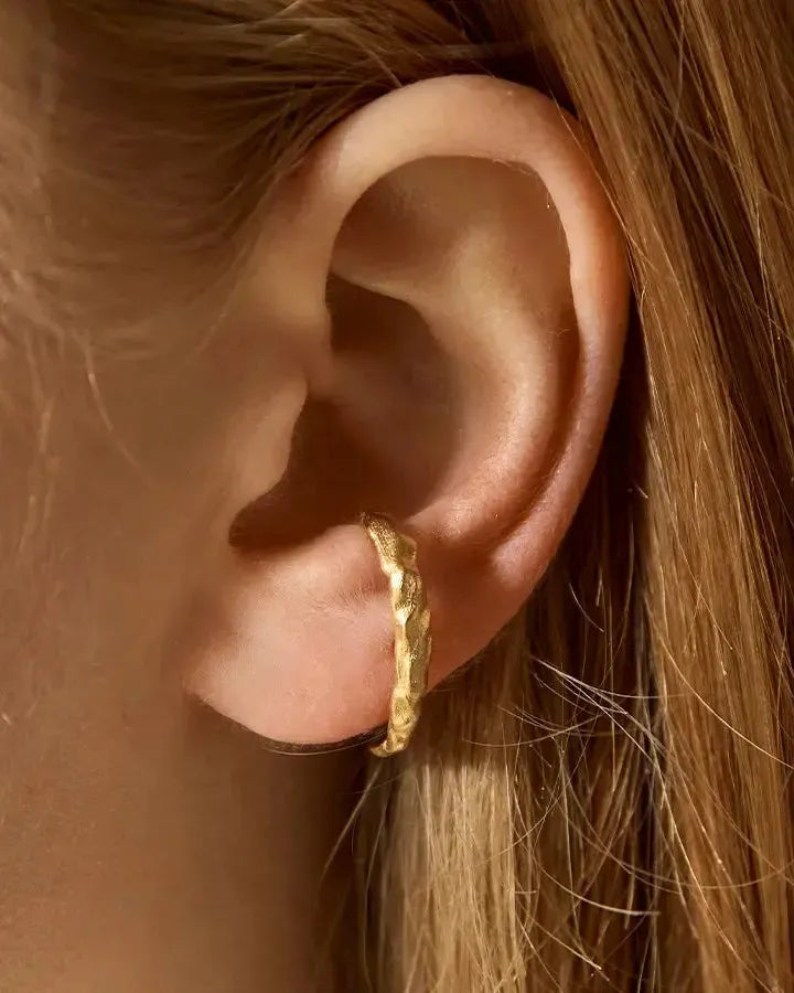 Eulalia gold half-hoop bar earrings with an irregular, textured finish worn on the second lobe.
