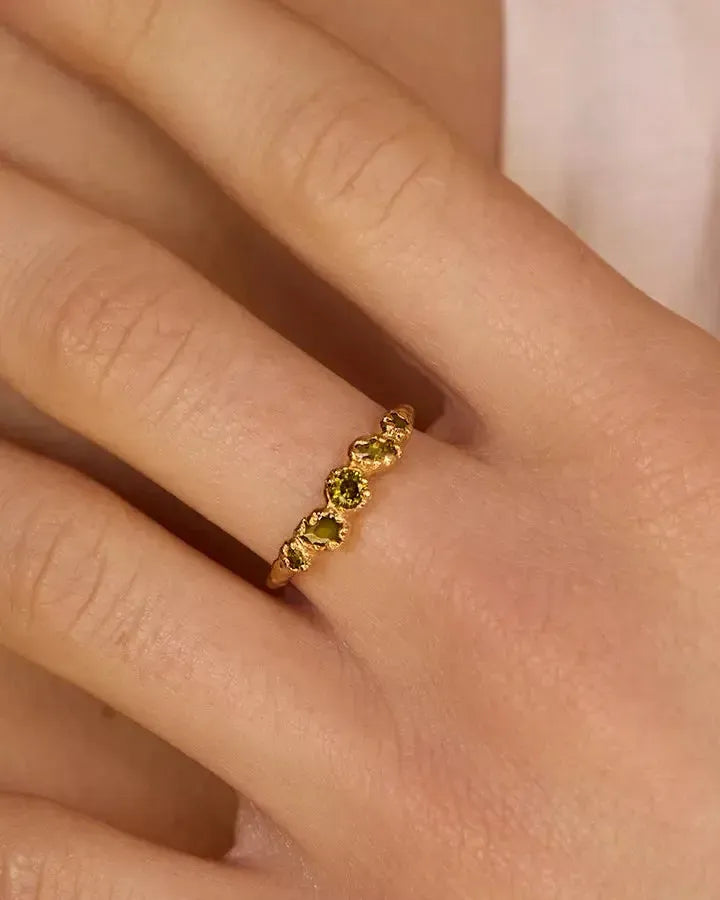 Koré slim gold cluster ring with five irregular dark green stones on a finger.