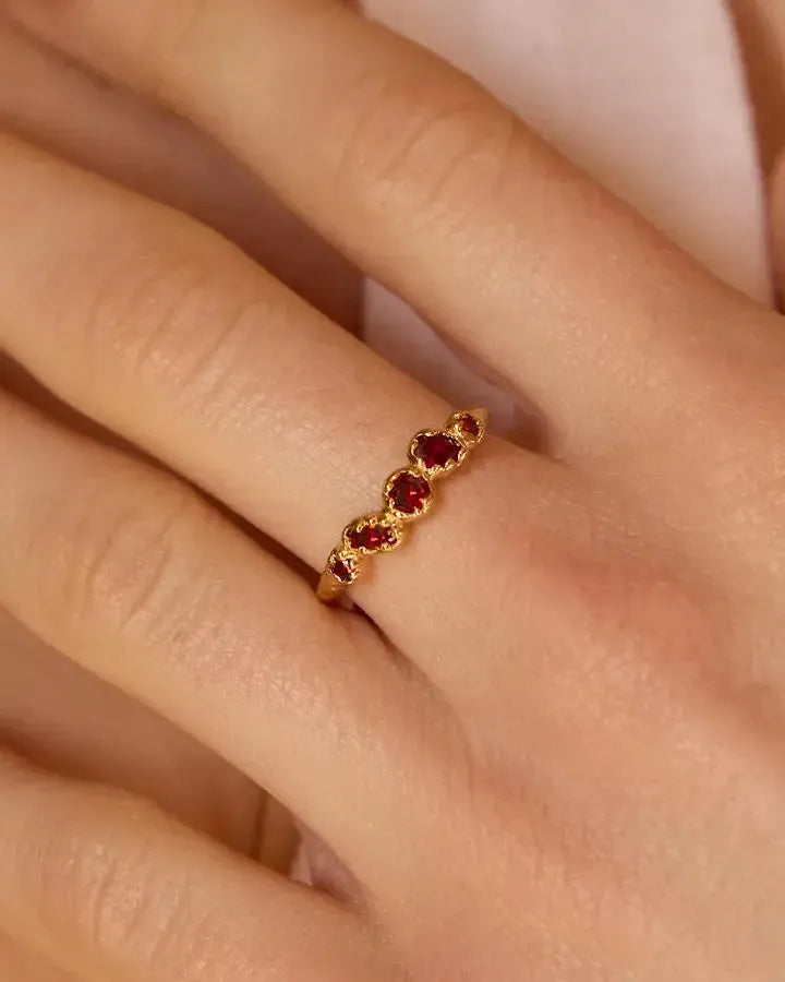 Koré Red Ring: Gold slim cluster ring with five irregular, handset red garnet stones on a finger.