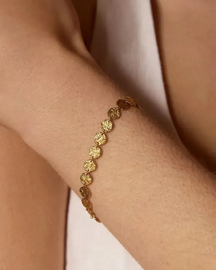 Caius bracelet with small, hammered gold discs on a woman's wrist.