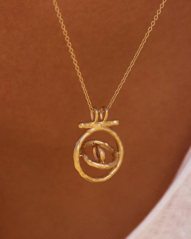 Collar Gali dorado con colgante de sol giratorio en un marco giratorio, puesto en una modelo.