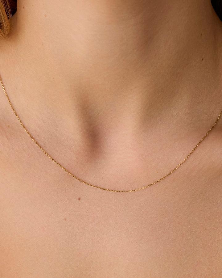 Proma gold cable chain necklace with small round links, worn on a person's neck.