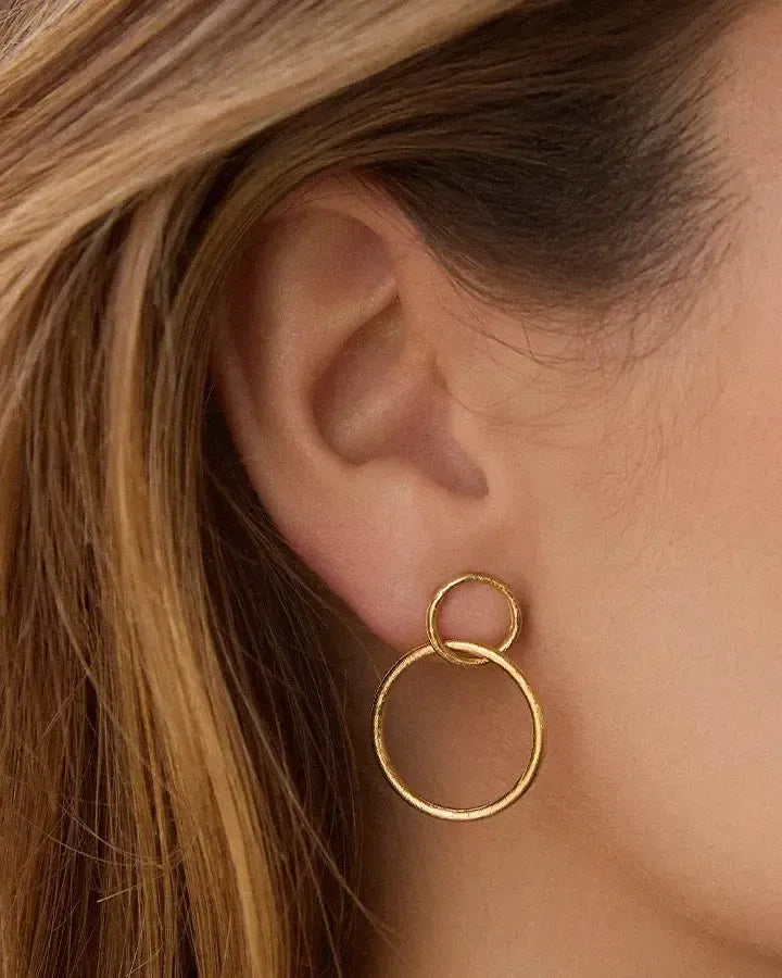 Selina gold-toned earrings featuring two interlocking circular hoops on an ear.