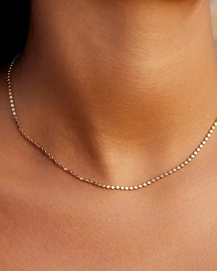 Delicate gold Anatole choker with small, flat, round links worn on a person's neck.