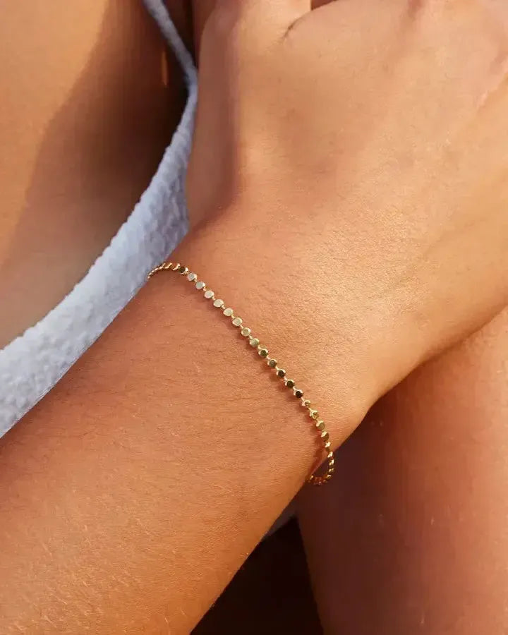 Delicate gold Anatole bracelet with small, flat circular links on a woman's wrist.