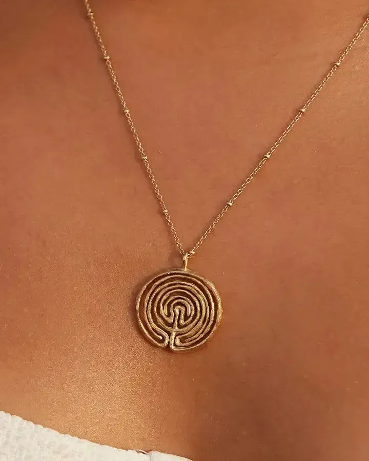 Collier Knossos doré avec pendentif labyrinthe rond sur une chaîne à perles délicate, porté sur la poitrine.