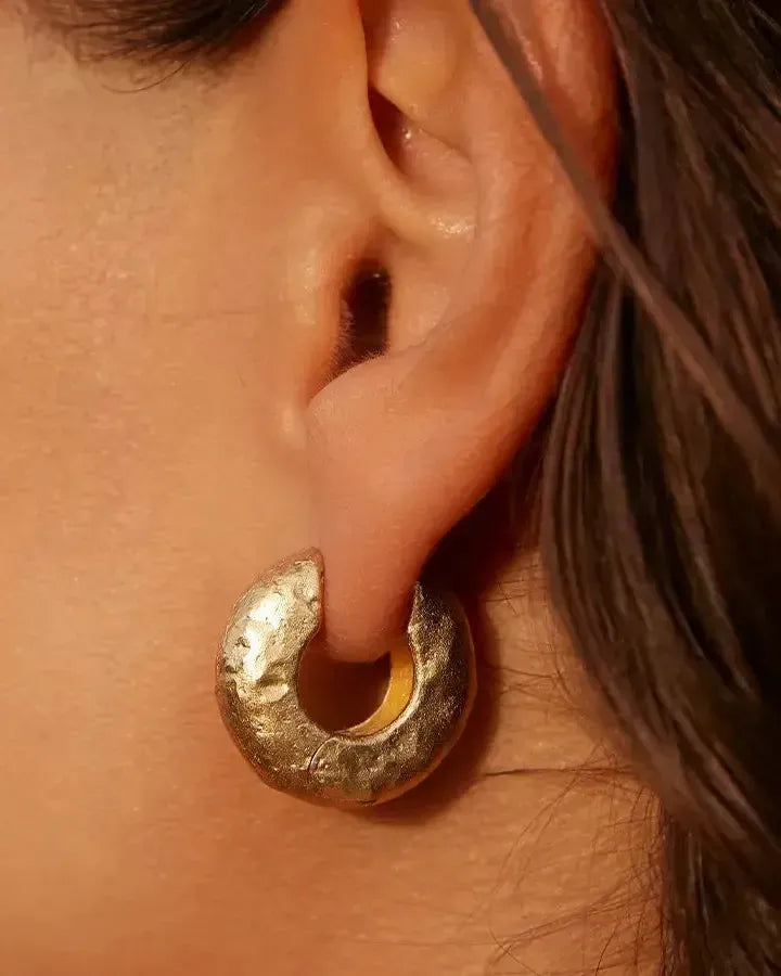 Close-up of a gold Anilla hoop earring with a hammered, textured finish on an ear.