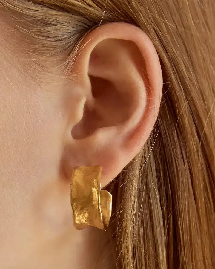 Lucca wide gold concave hoop earring with hammered matte exterior and polished interior, worn on an ear.