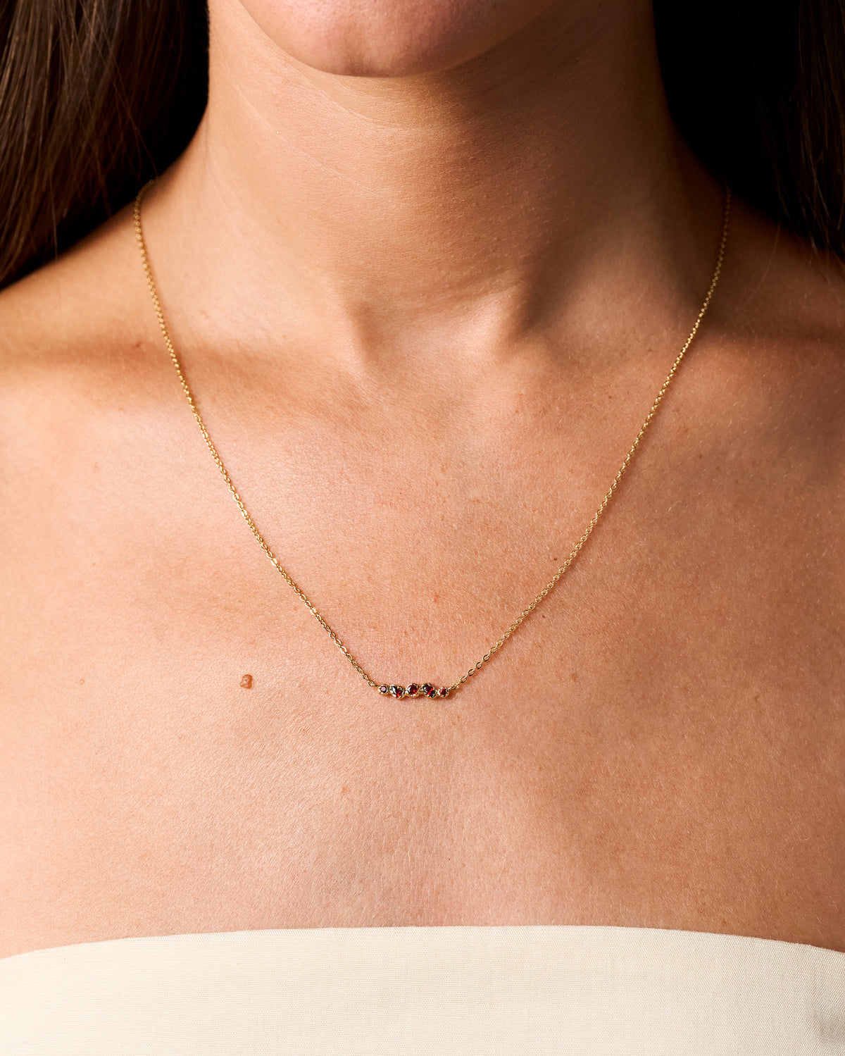 Delicado collar de cadena dorado con cinco pequeñas piedras rojo intenso en un engaste orgánico e irregular, en el cuello.