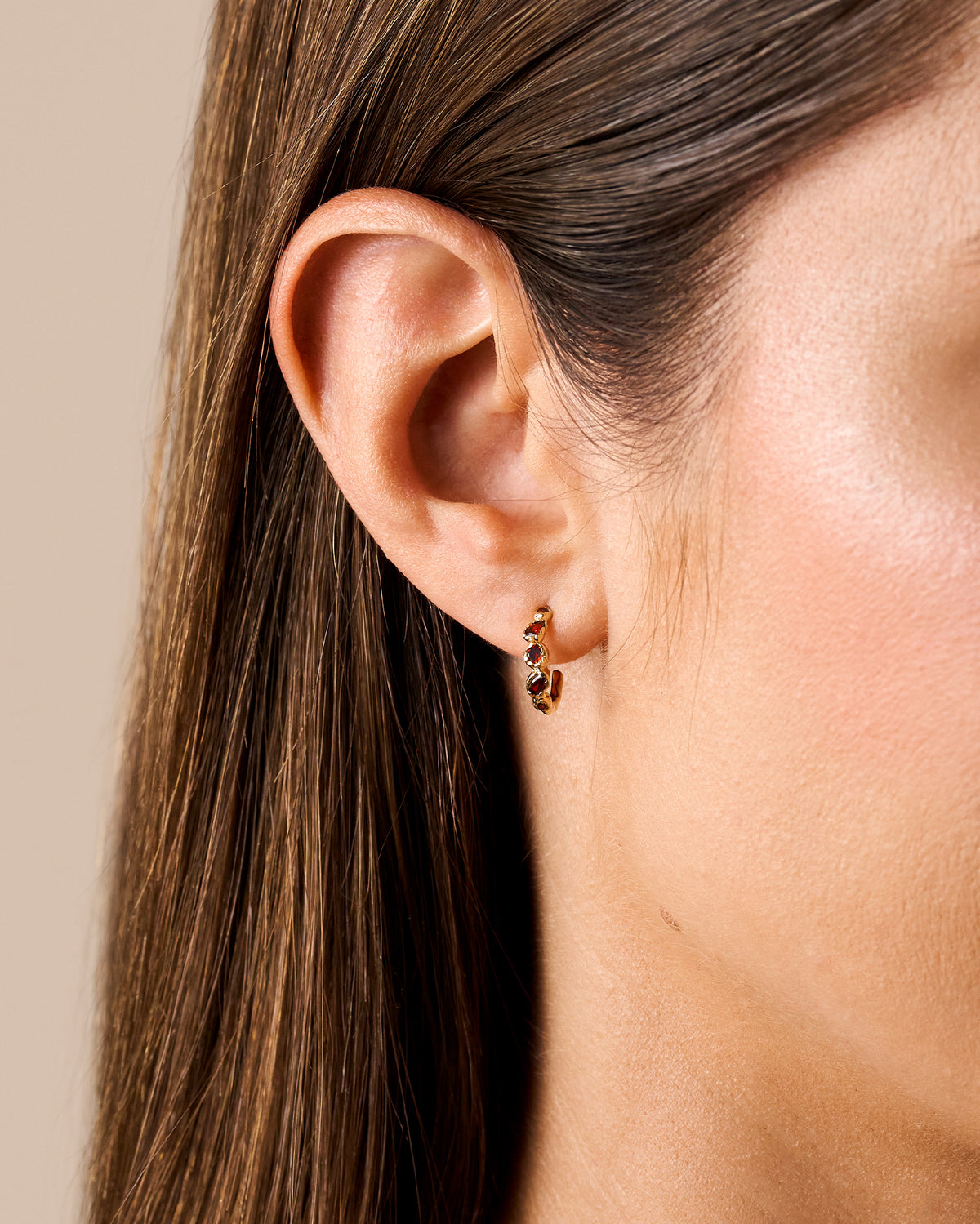 Small gold hoop earrings featuring five deep red stones in a textured, antique-inspired setting worn on an earlobe.