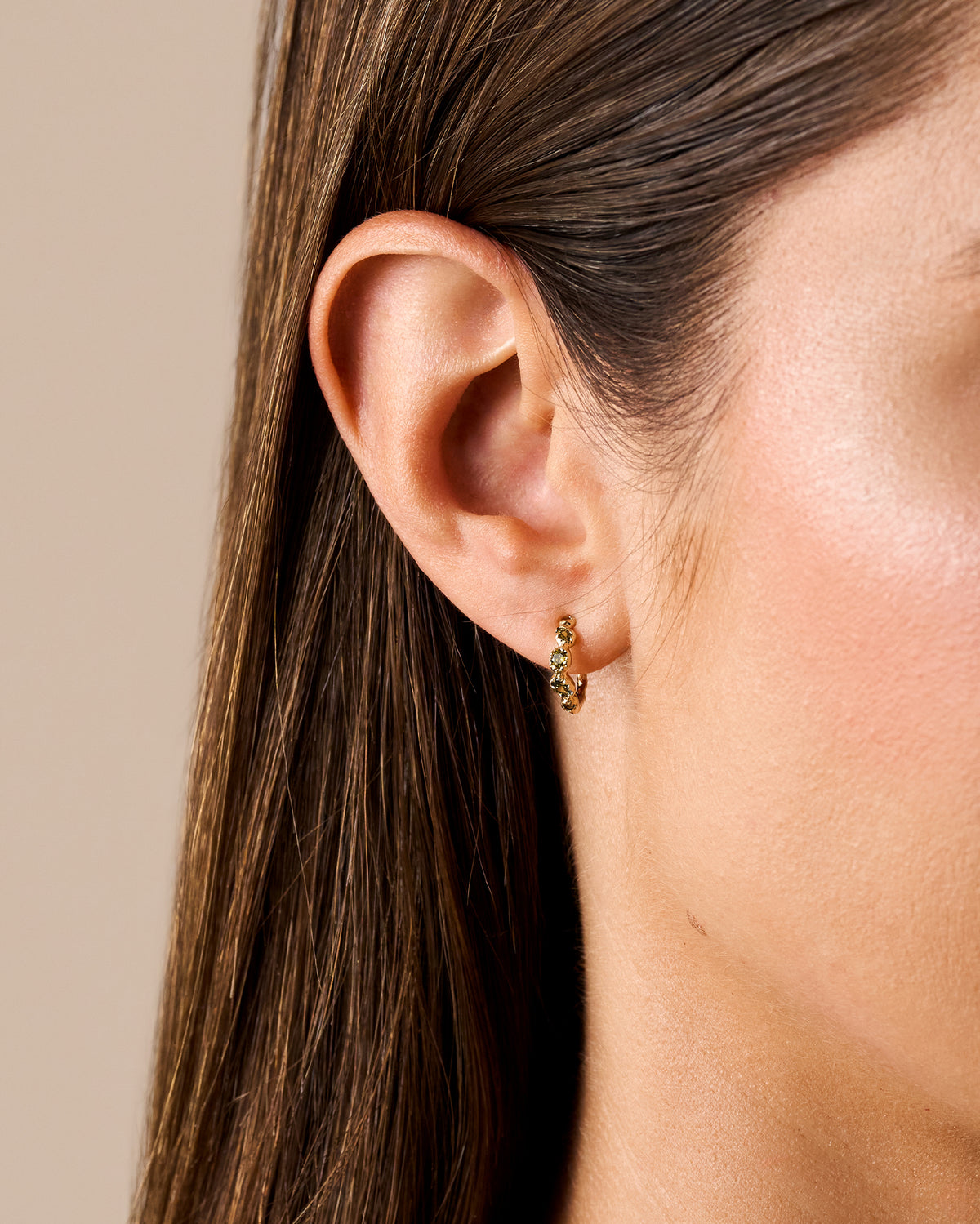 Small gold hoop earring featuring five deep green stones in a textured, antique-inspired setting worn on an earlobe.