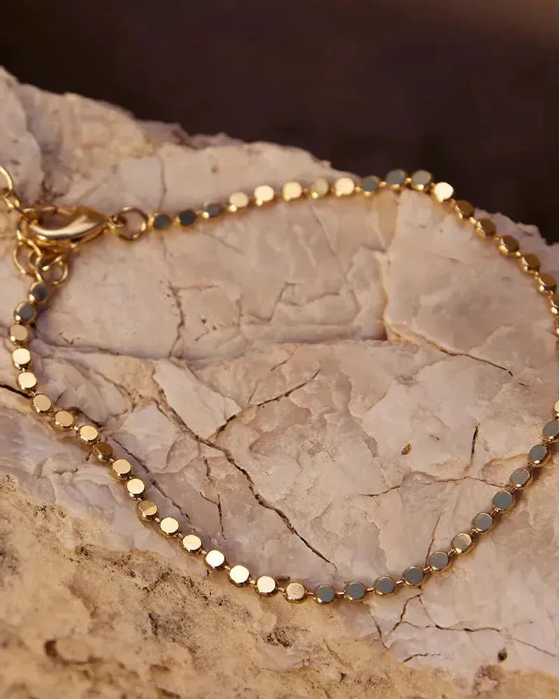 Delicate gold Anatole bracelet with small, flat, round links on a textured white rock.