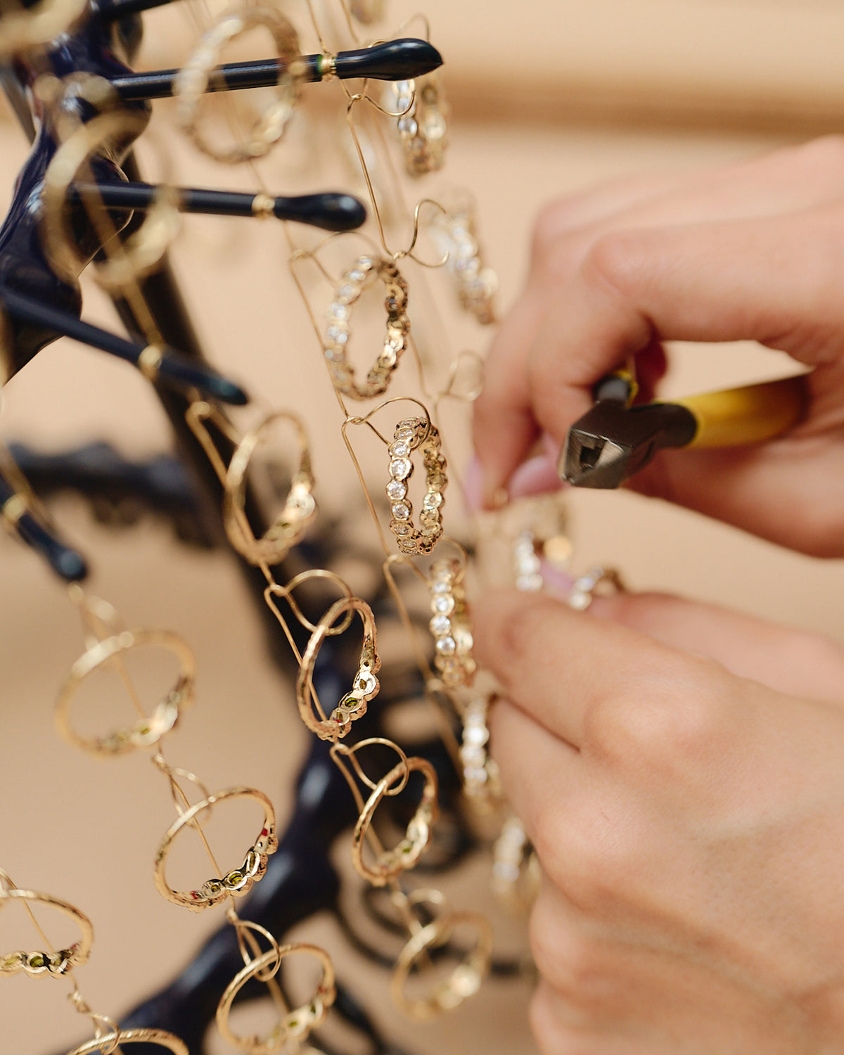 Jeweler using pliers to adjust gold hoop earrings with sparkling stones hanging on a display stand.