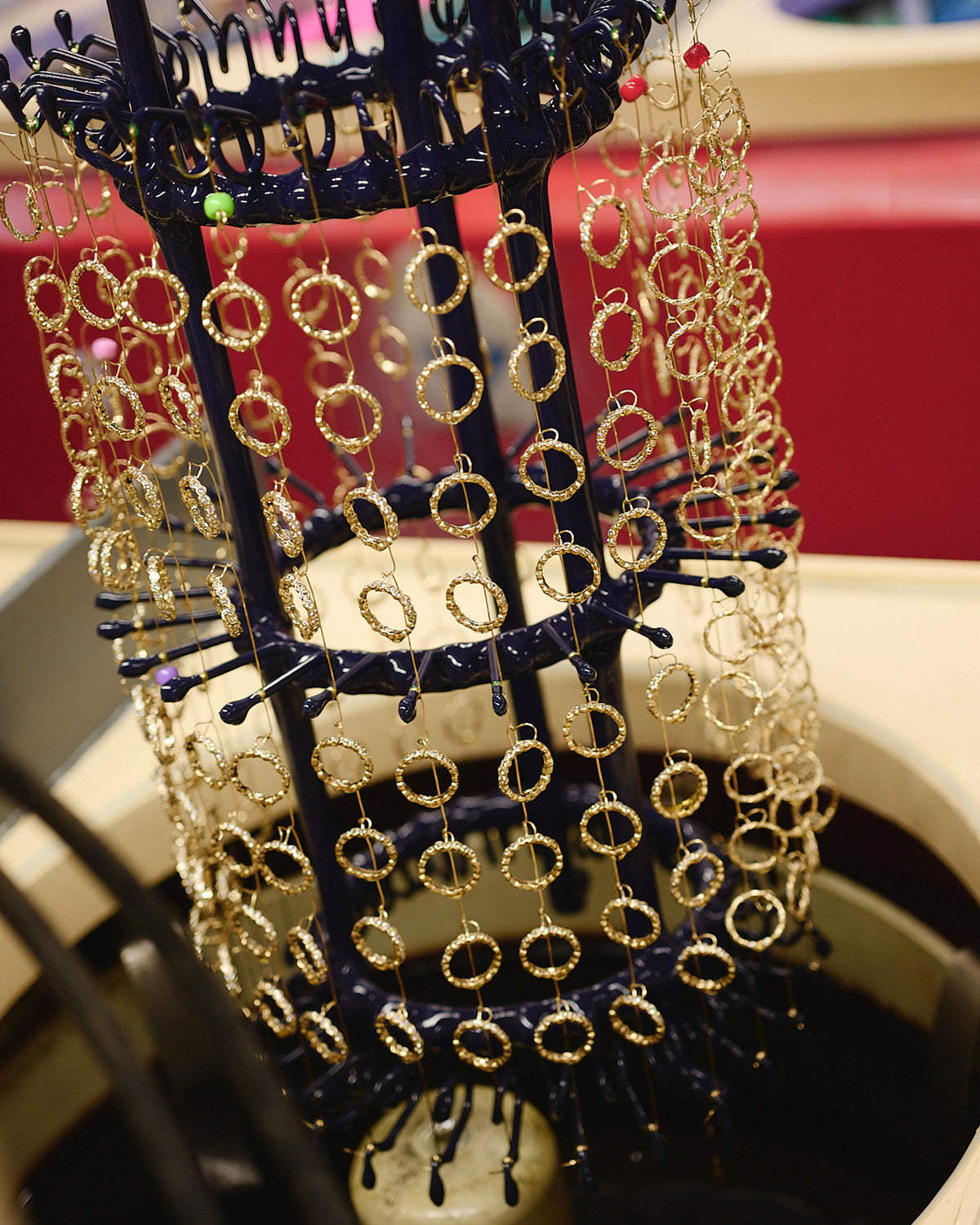 Gold hoop earrings hanging on a dark blue industrial rack for jewelry plating or manufacturing.