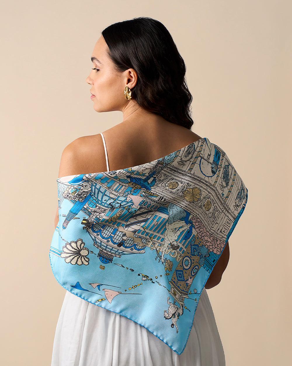 Woman wearing an Atlantis silk scarf with blue Mediterranean-inspired art, corals, and jewelry designs.