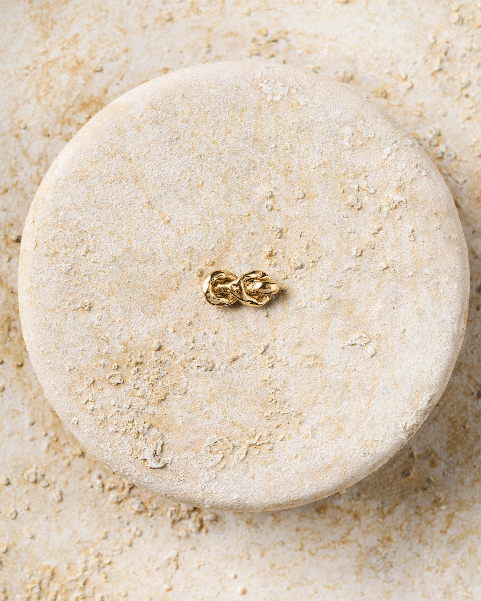 Gold hammered knot piercing stud with two interlocking rope-like strands and a flat-back closure.