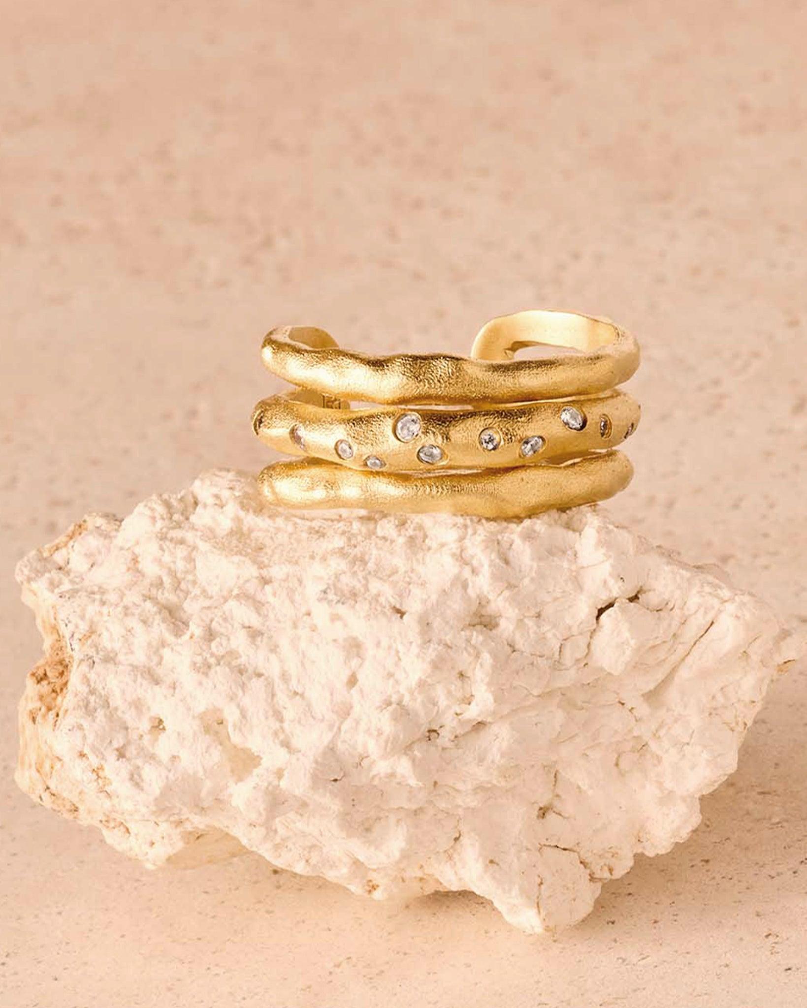 Goldfarbener Iris Ring mit drei unregelmäßigen Ringbändern, das mittlere mit weißen Steinen verziert.