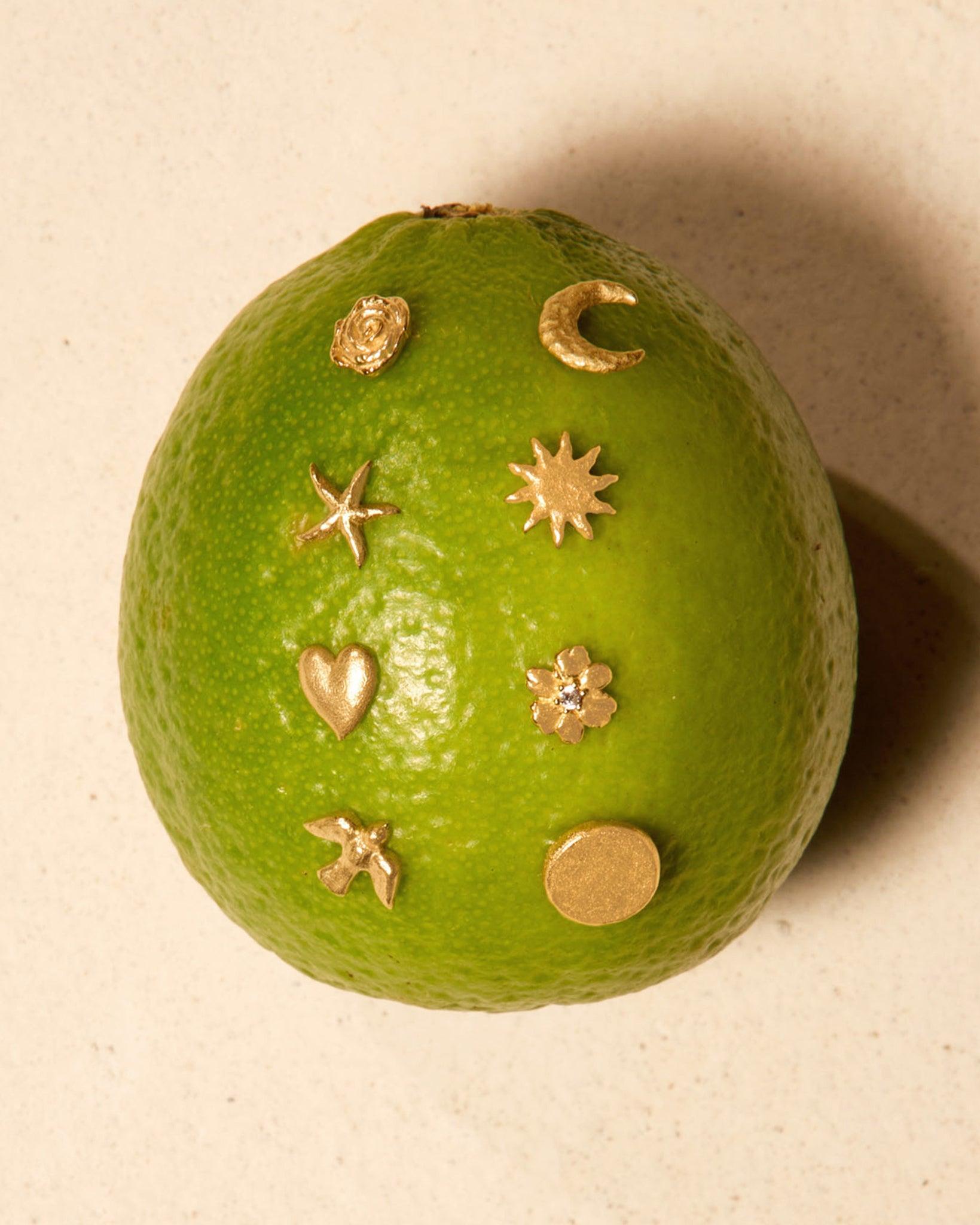 Assorted small gold stud earrings in various shapes like star, moon, heart, flower, and circle on a lime.