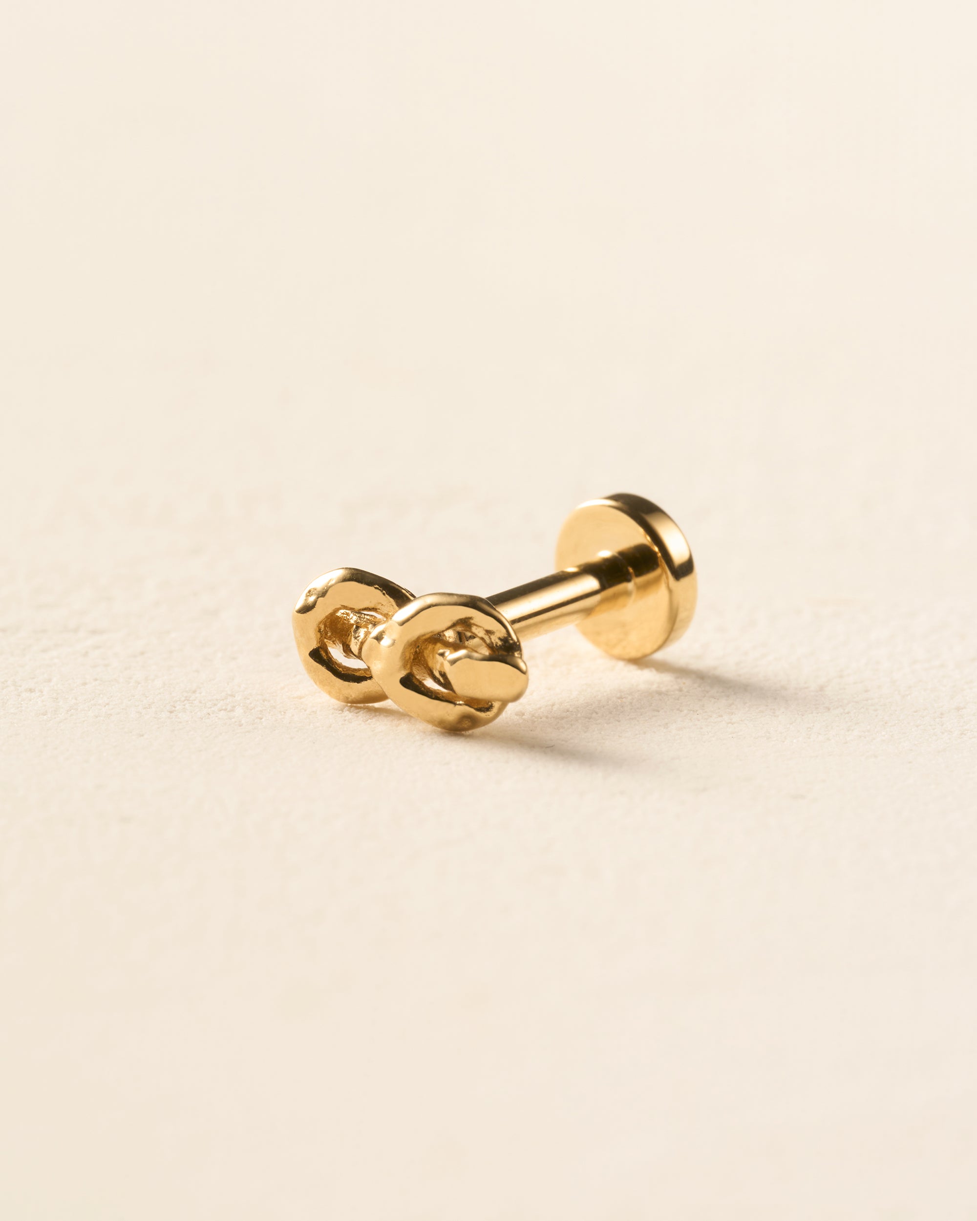 Gold hammered knot piercing stud with two rope-like strands and a flat-back closure.
