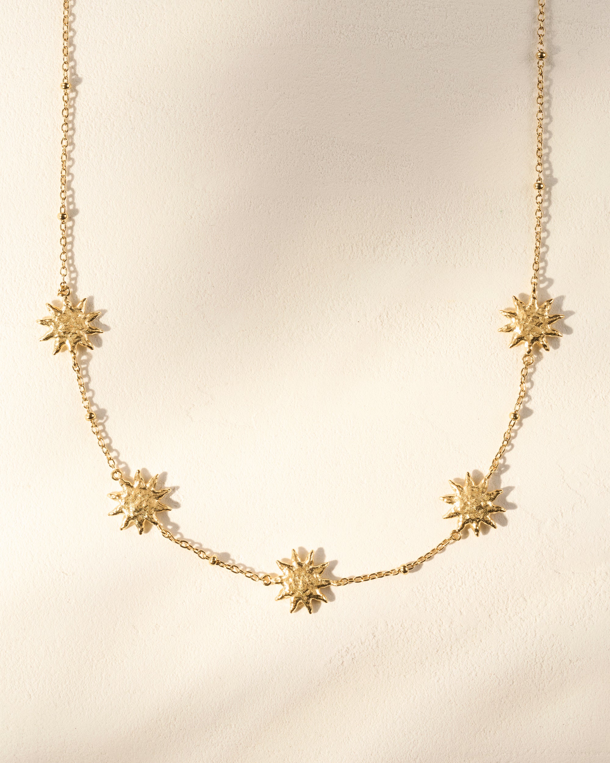 Gold Soléos necklace with five sculpted, hammered sun charms on a fine chain.