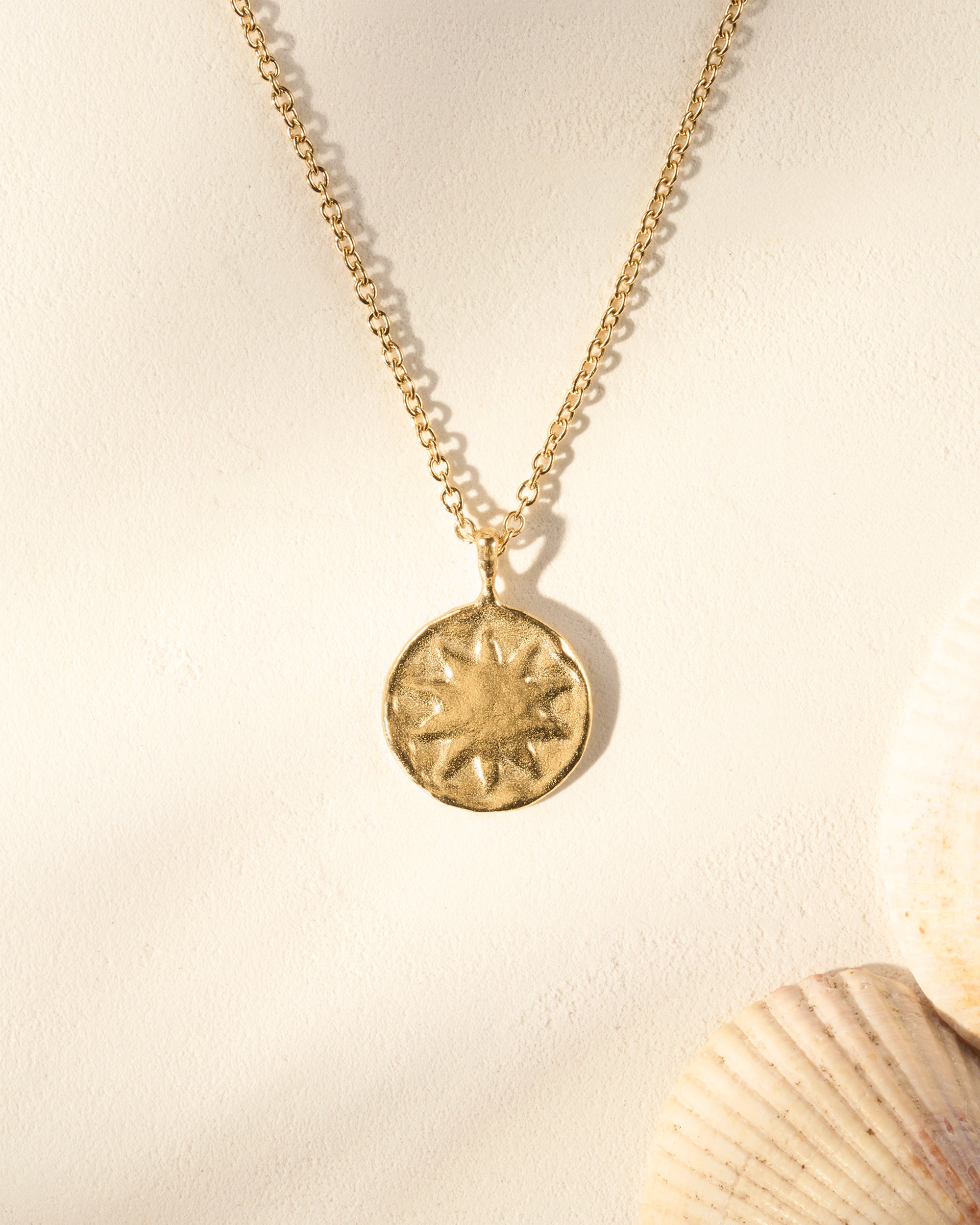Gold Soléia necklace with an irregular sun medallion pendant on a fine chain, hammered surface.