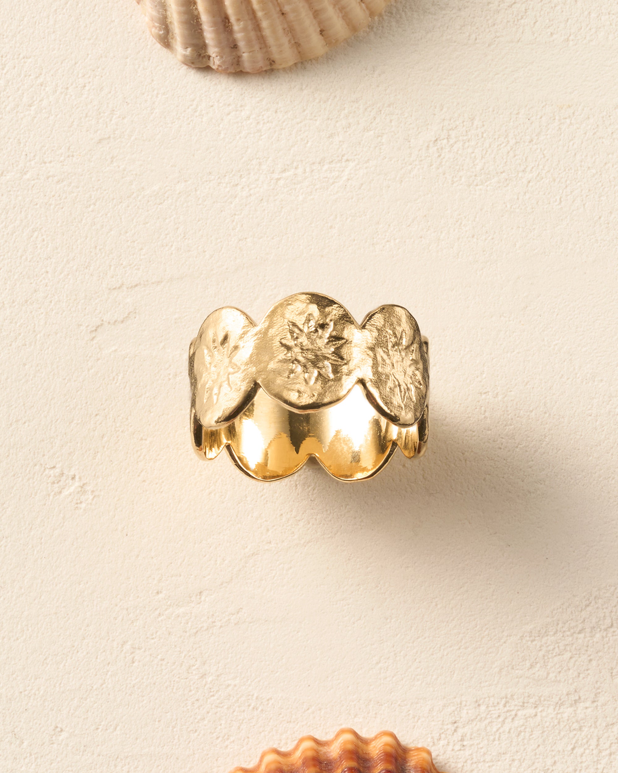 Gold Soléos ring with a wide hammered band, scalloped edges, and engraved sun motifs.