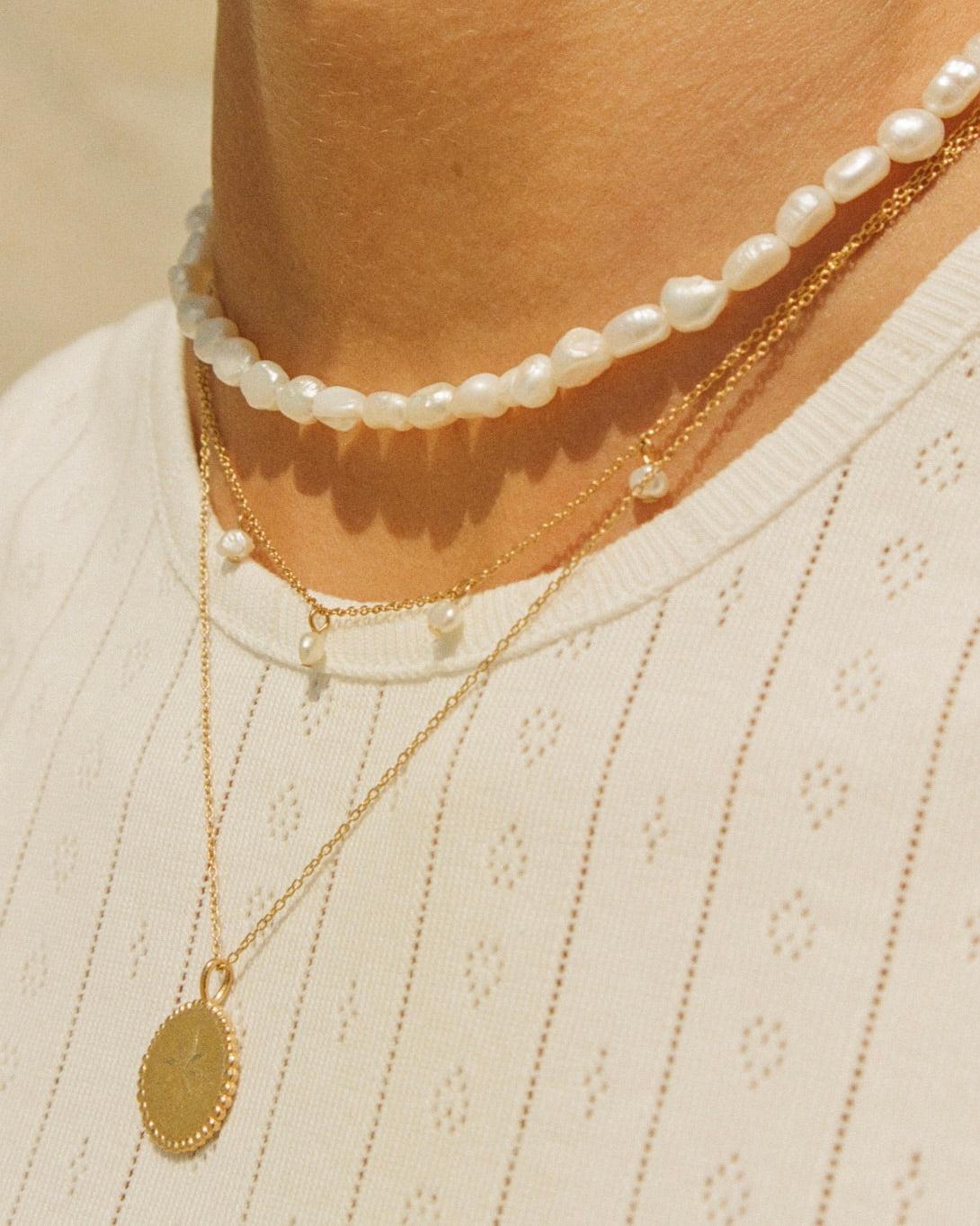 Estée Choker: Dainty gold layered necklaces with irregular white pearls and a round gold pendant.