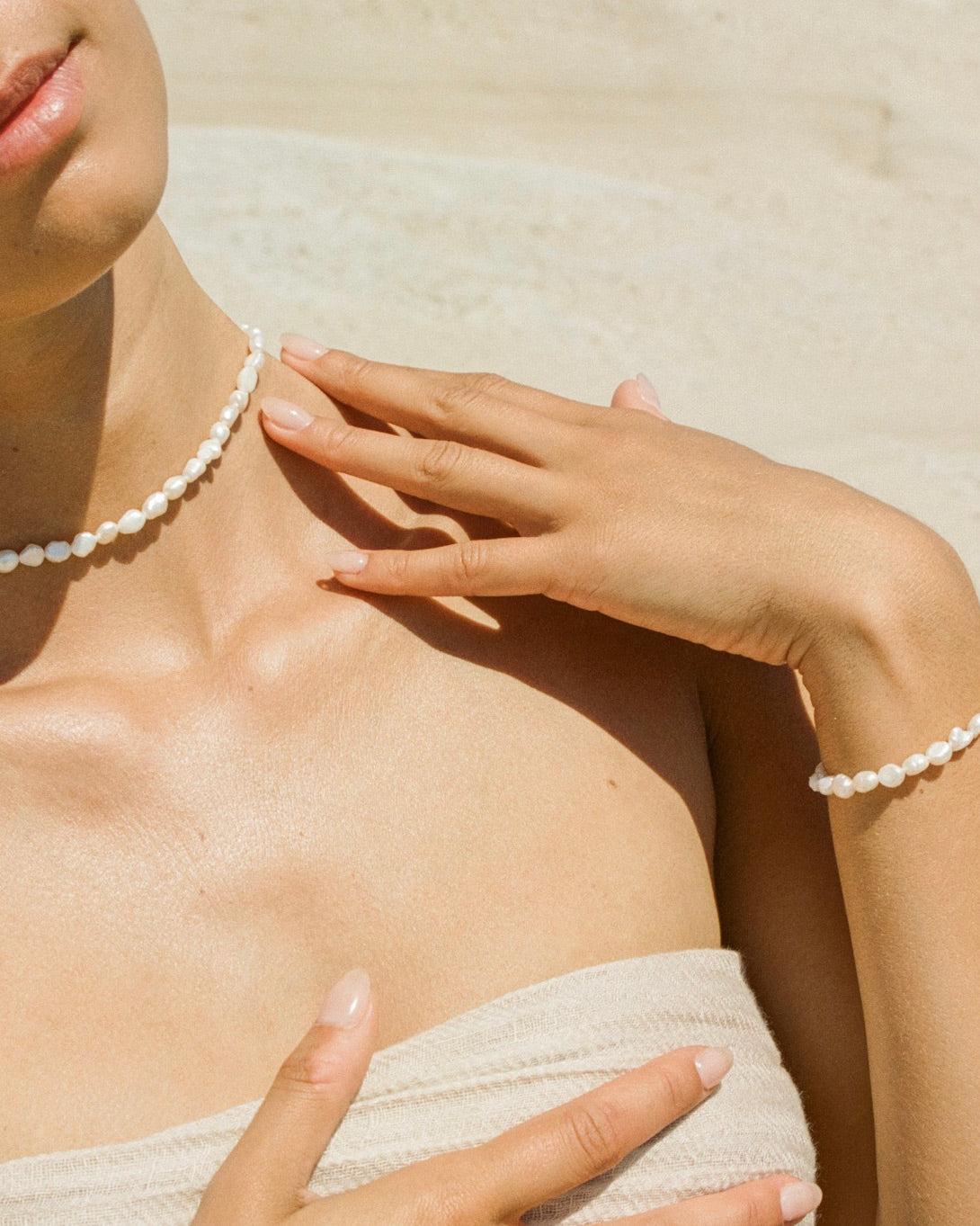 Dainty Estée choker and matching bracelet with small white pearls on a woman's neck and wrist.