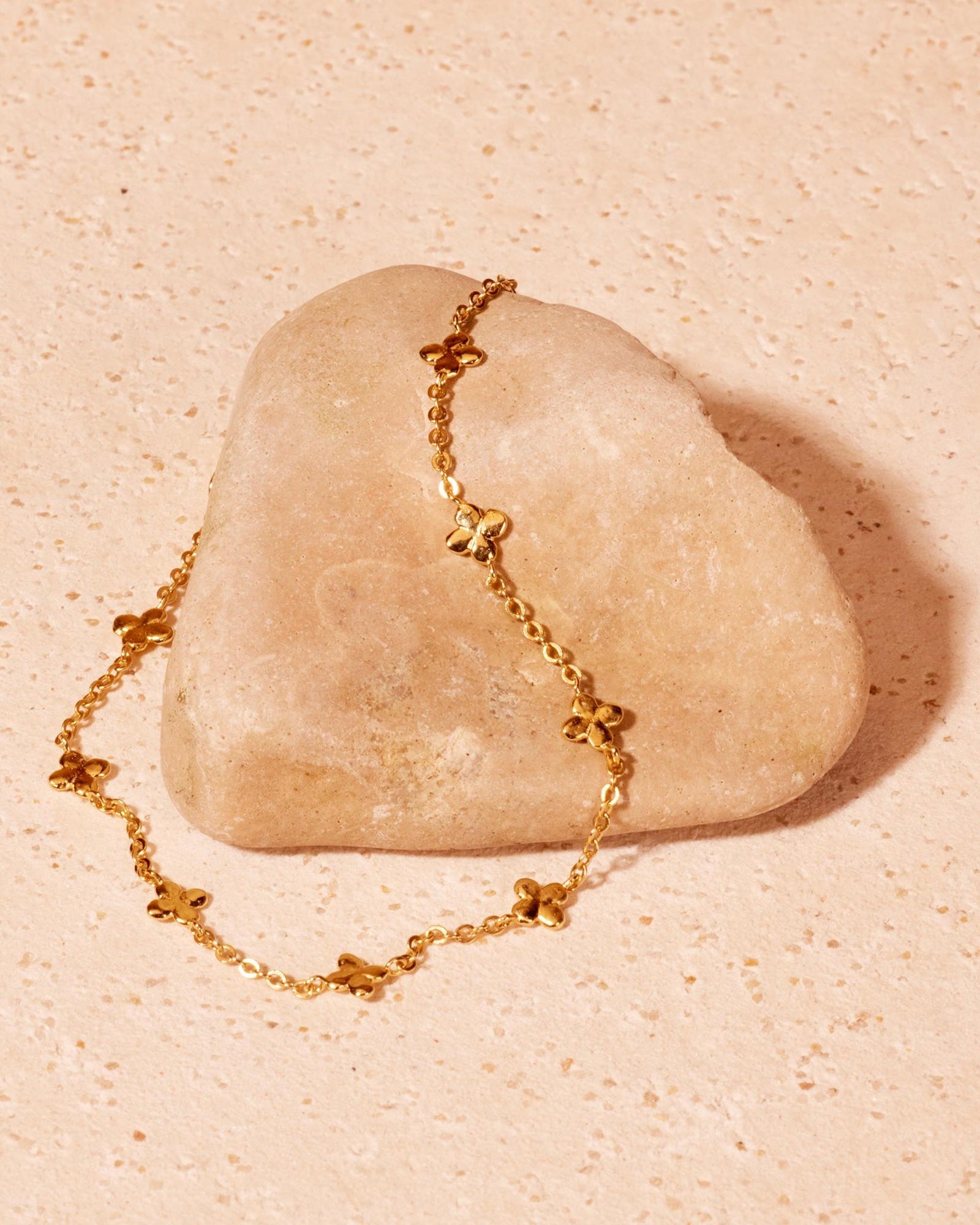 Golden Laeta bracelet with small, irregular four-leaf clovers on a fine chain, draped over a light stone.