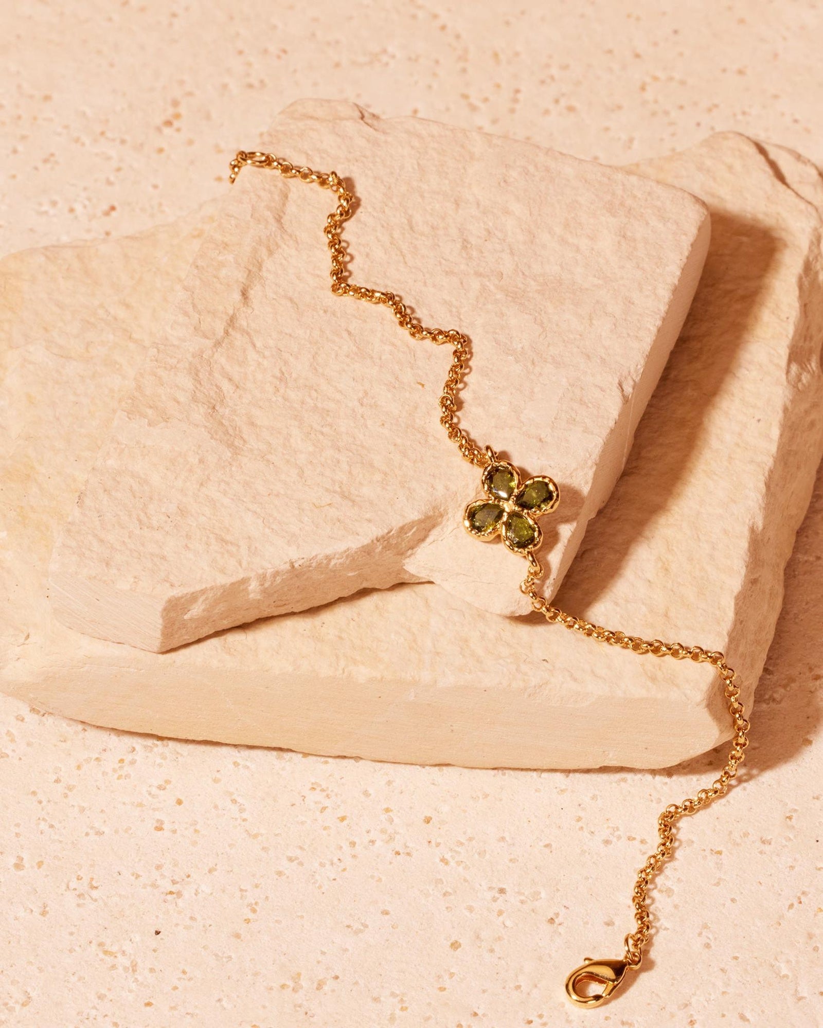 Fausta gold chain bracelet with a four-leaf clover charm, each leaf a deep green pear-cut stone.