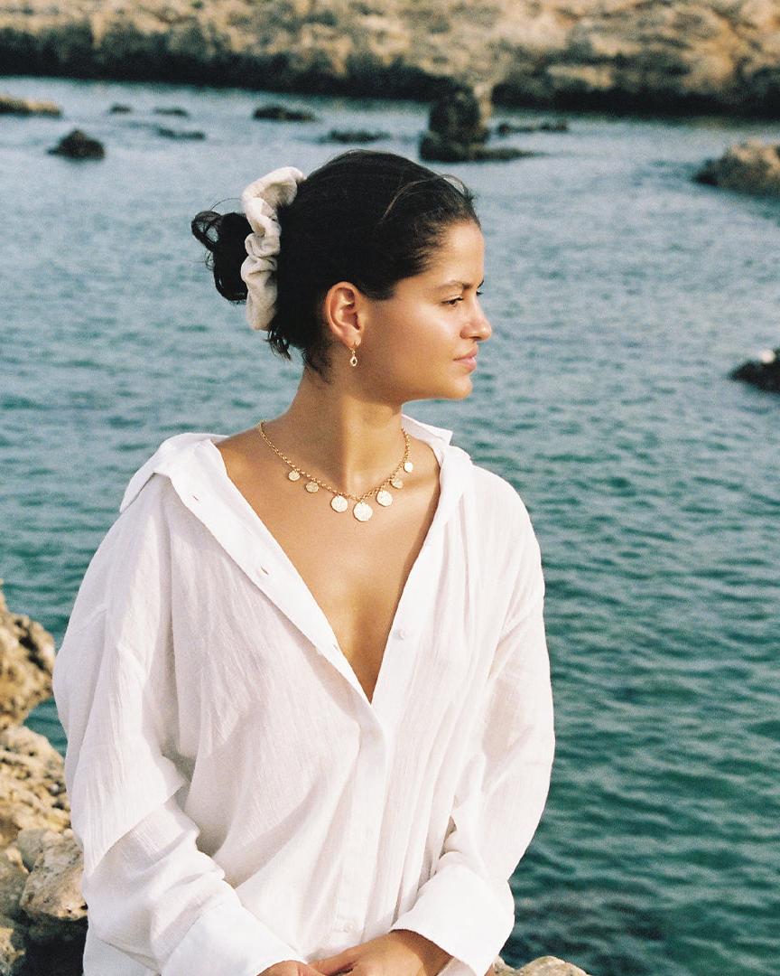 Cassius necklace with 7 hammered golden circles on a statement chain, worn by a woman in a white shirt.