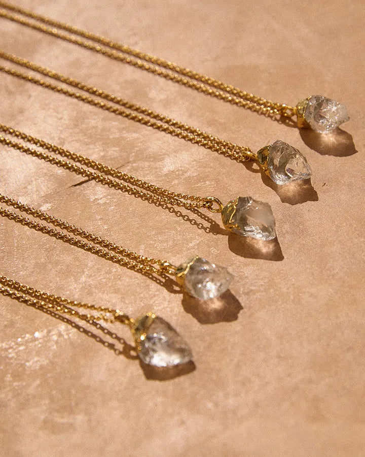 Five Dioné necklaces with clear quartz pendants in irregular gold settings on slim gold chains.
